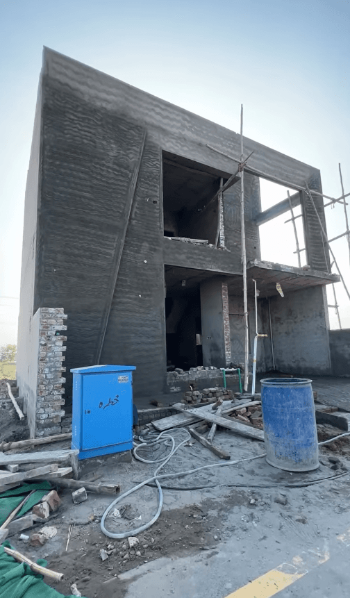 Two-story building under construction with textured grey plaster, scaffolding, and a blue utility box.