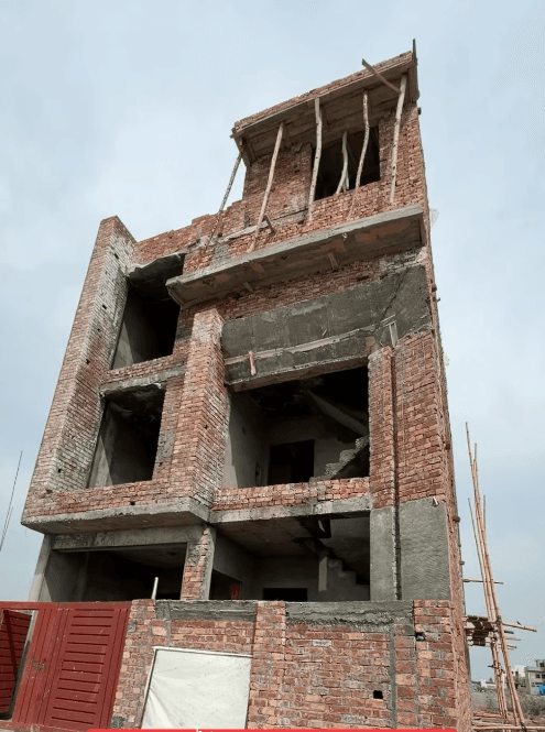 Tall red brick building under construction with open window spaces and wooden supports on top.