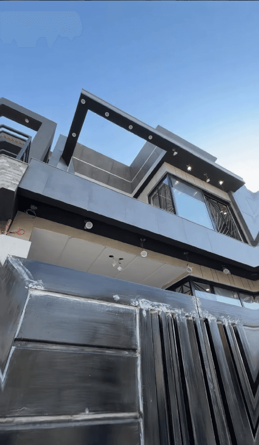 Modern multi-story house with dark grey facade, large windows, and a black metal gate.