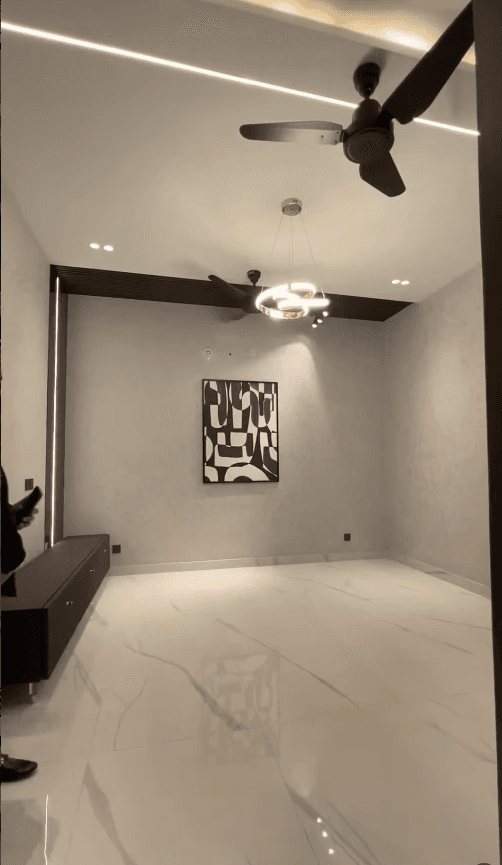 Modern minimalist room with marble floors, abstract wall art, black ceiling fans, and contemporary lighting.