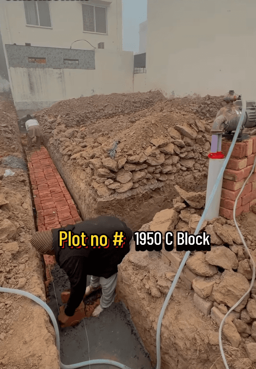 Workers laying red bricks in a foundation trench for Plot no # 1950 C Block.