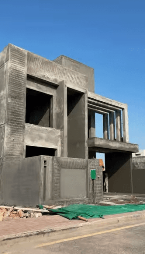 Modern gray concrete house under construction with large rectangular openings under a blue sky.