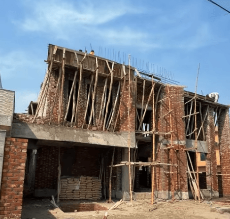 Red brick building under construction with wooden scaffolding and support poles against a blue sky.