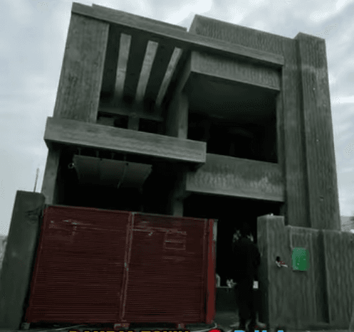 Modern two-story concrete house under construction with a red gate and textured exterior walls.